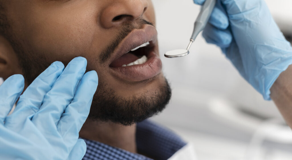 Dentist hands in gloves checking black man mouth
